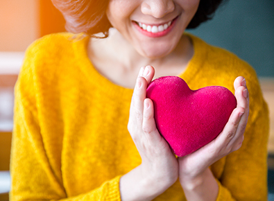 woman in yellow shirt holding heart pillow